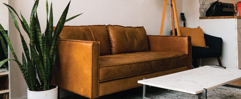 Um sofá grande com um tom alaranjado criando mais cor no ambiente junto de uma almofada em um tom de cor próximo.